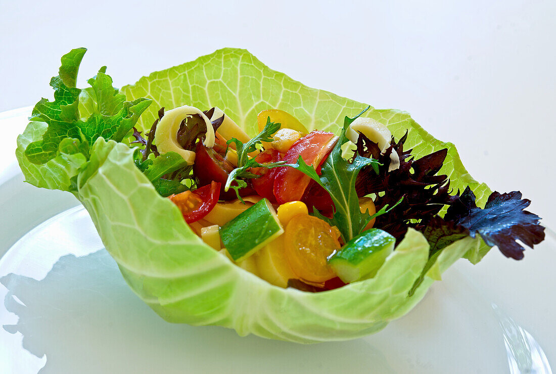 White cabbage leaf bowl with mixed vegetable salad and herbs