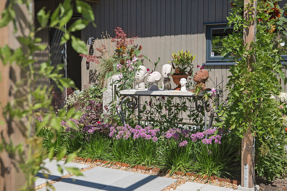 Gepflegter Vorgarten mit Blumenbeeten und dekorativem Skulpturentisch