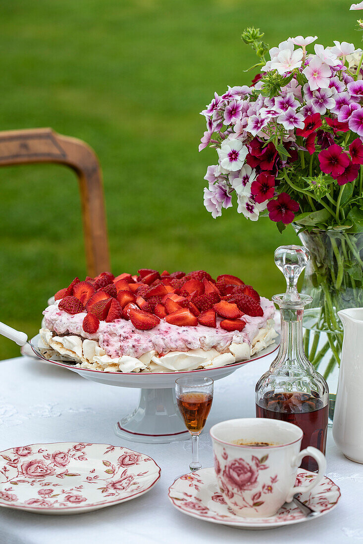 Strawberry cake, coffee service and bouquet of petunias on garden table