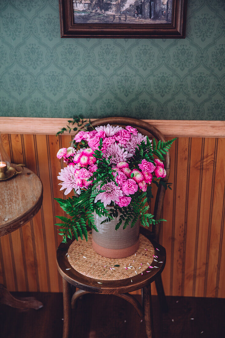 Rosa Blumenstrauß aus Herbstchrysanthemen (Chrysanthemum), Nelken (Dianthus), und Farnblätter auf einem Stuhl