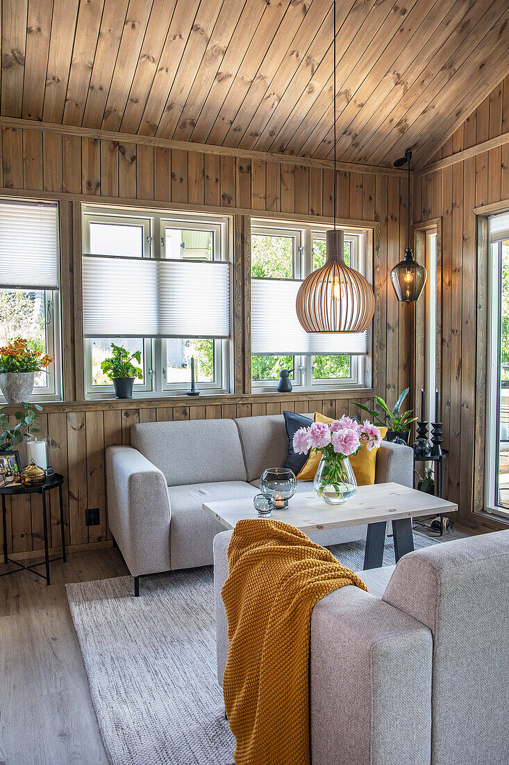 Grey sofas and wooden table with bouquet of flowers in wood-panelled living room