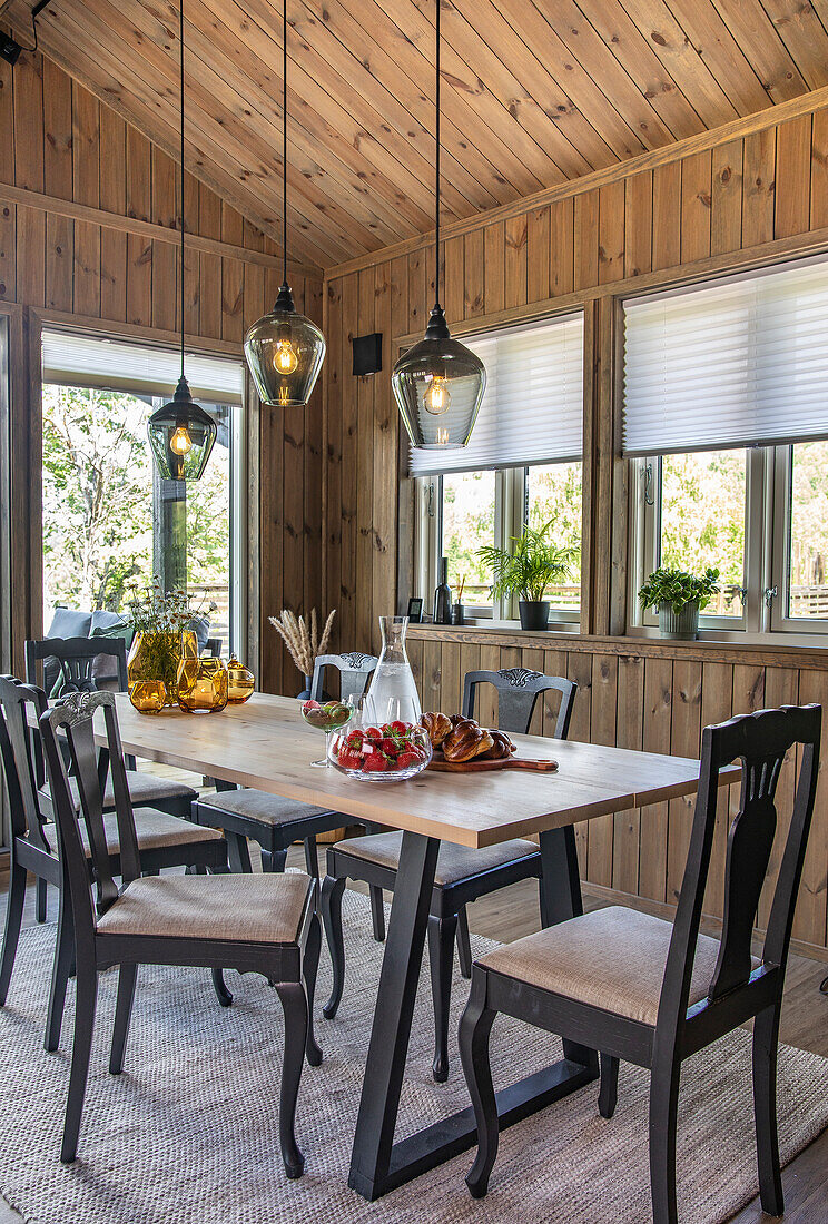 Wooden table and black chairs in dining area, wood panelling and pendant lights