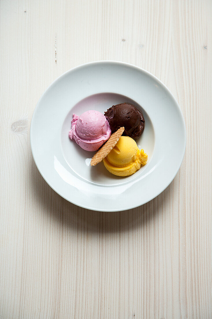 Three ice cream scoops (raspberry, chocolate and mango) with ice cream cone