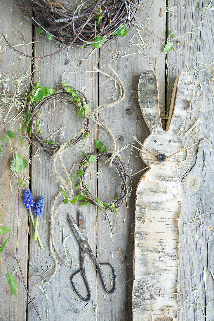 Osterhase ausgeschnitten aus Birkenrinde mit Kränzchen aus Birkenzweigen und Traubenhyazinthen (Muscari), Osterdekoration auf der Terrasse