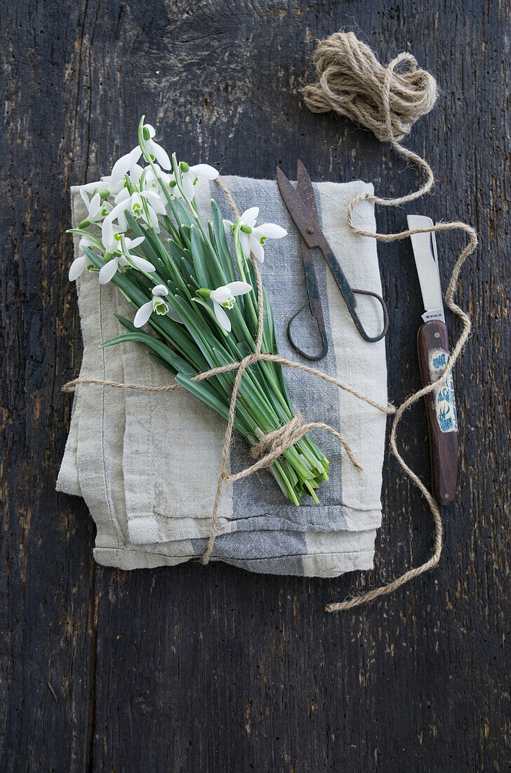 Strauß aus Schneeglöckchen (Galanthus) mit Schnur auf Leinenserviette