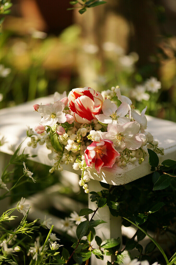 Strauss aus Apfelblüten, Tulpen (Tulipa) und Maiglöckchen (Convallaria) auf Gartentisch liegend