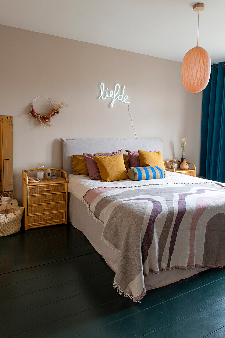 Bedroom with rattan furniture, colored throw pillows and neon lettering on the wall