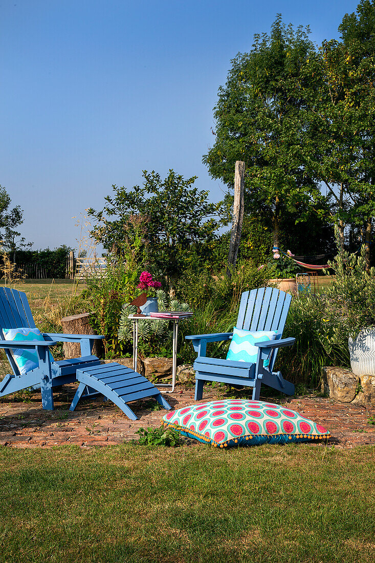 Blaue Gartenstühle mit buntem Kissen auf einer Rasenfläche im Sommer