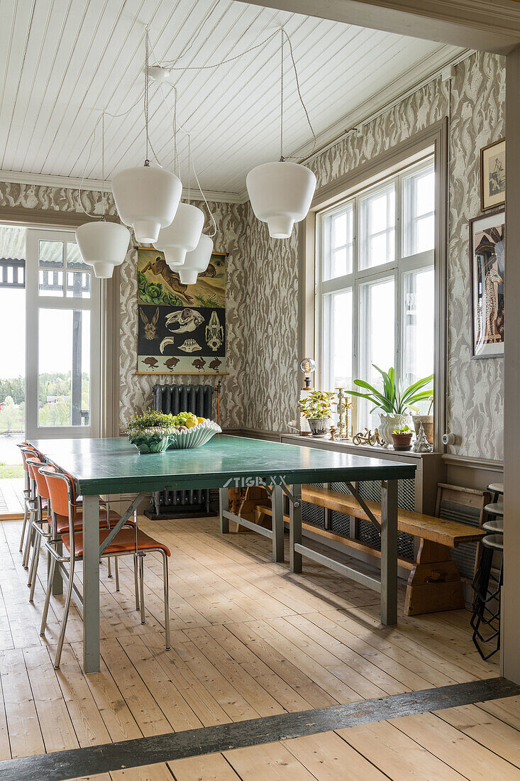 Dining room with green wooden table, orange-colored chairs and white pendant lights