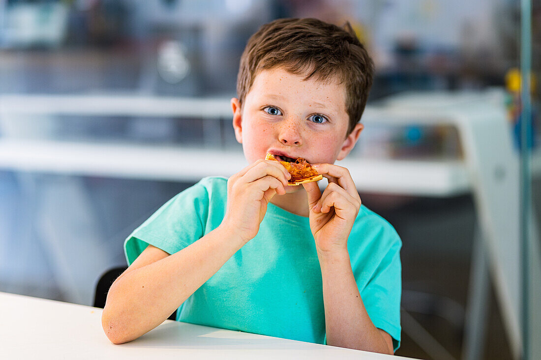 Junge in türkisblauem T-Shirt isst ein Stück Pizza