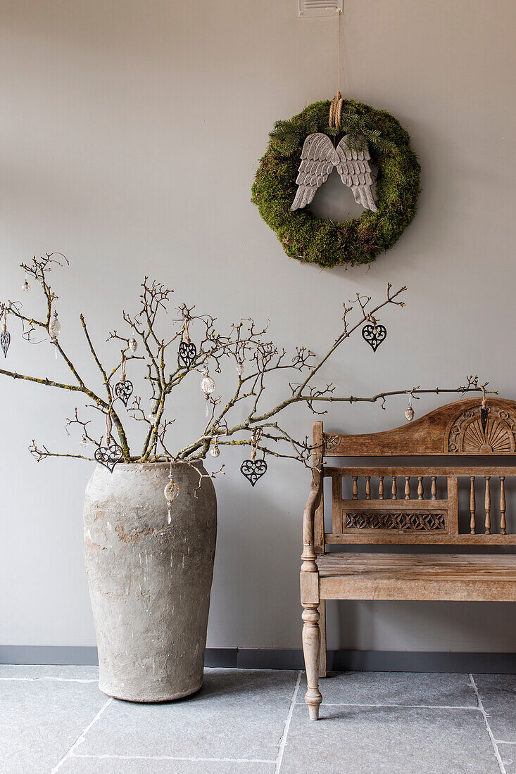 Wooden bench and decorative tree branch in vase with moss wreath on the wall