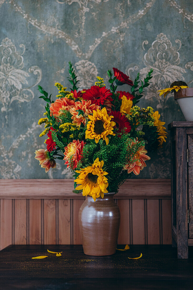 Herbstlicher Blumenstrauß aus Dahlien (Dahlie) und Sonnenblumen (Helianthus) vor alter Tapete