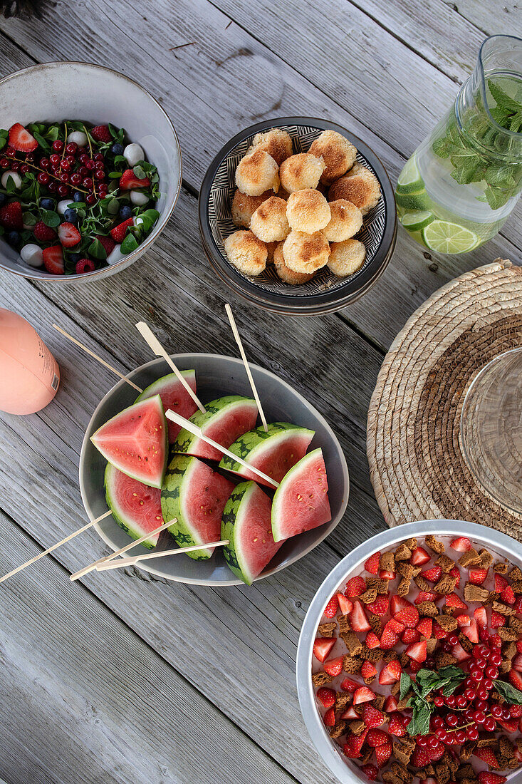 Sommerlicher Picknicktisch mit Wassermelonenspießen, Erdbeer-Dessert und Salat