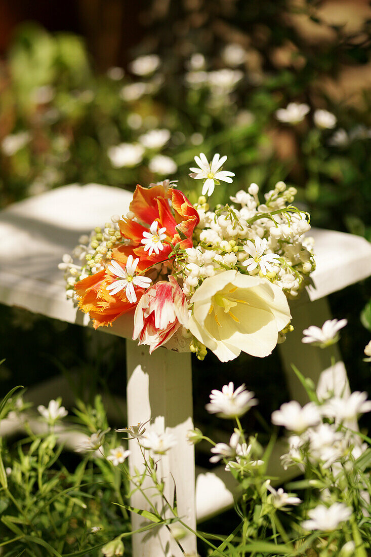 Bouquet of tulips (Tulipa) and lily of the valley (Convallaria) on a stool in the garden