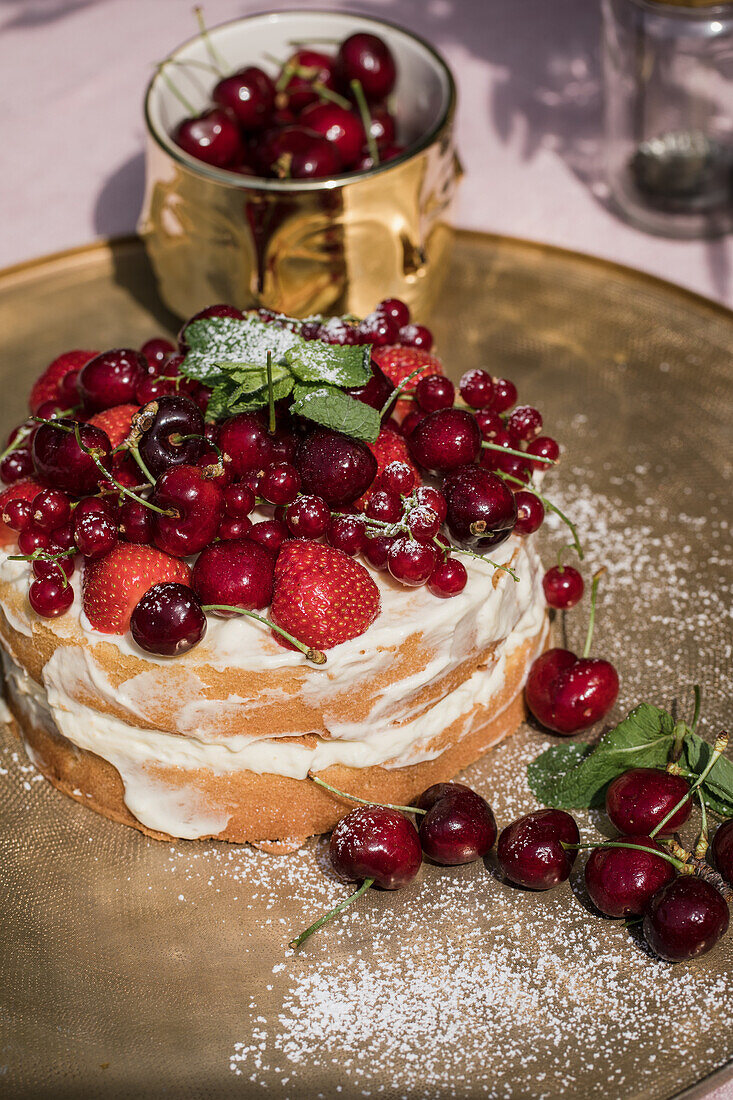 Sponge cake with fresh cherries, strawberries and redcurrants on a golden platter