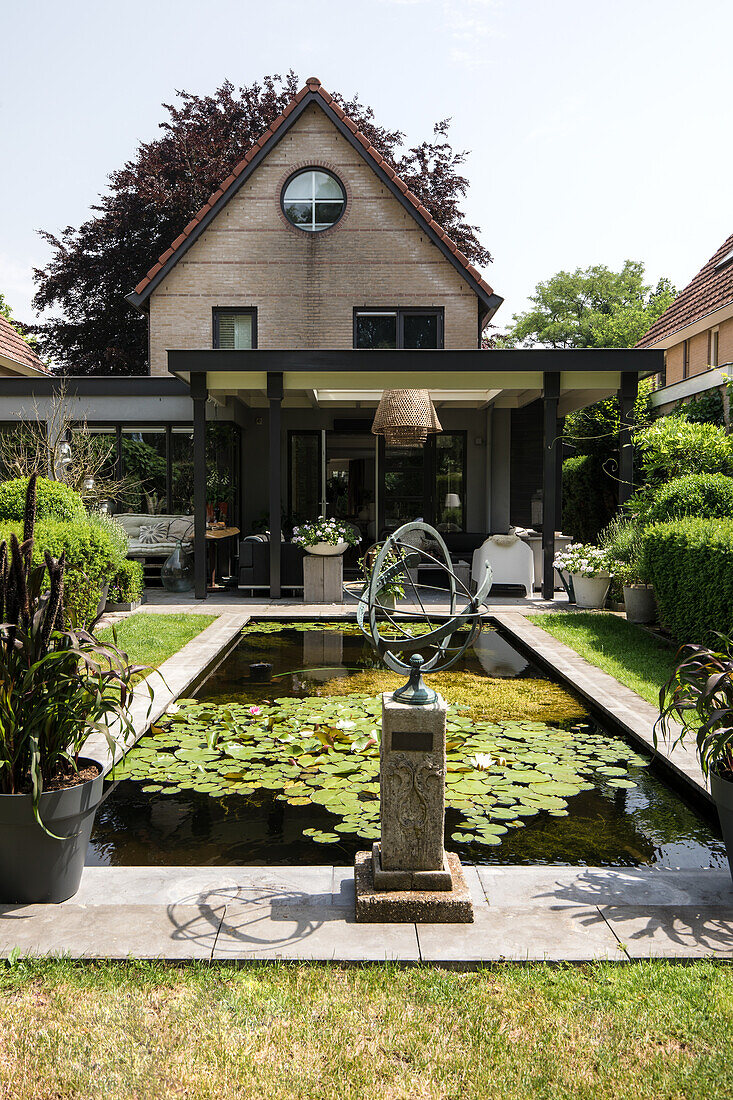 Modern garden with water lily pond and sundial in front of a detached house