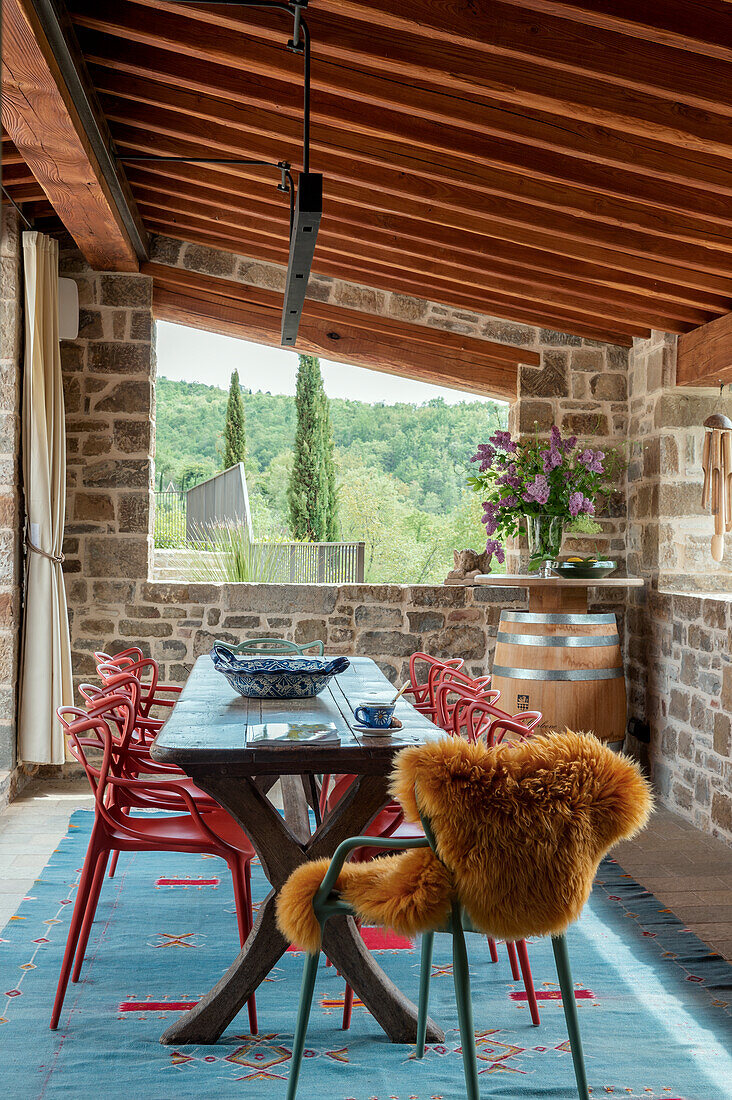 Dining area on covered terrace with stone walls and wooden beamed ceiling