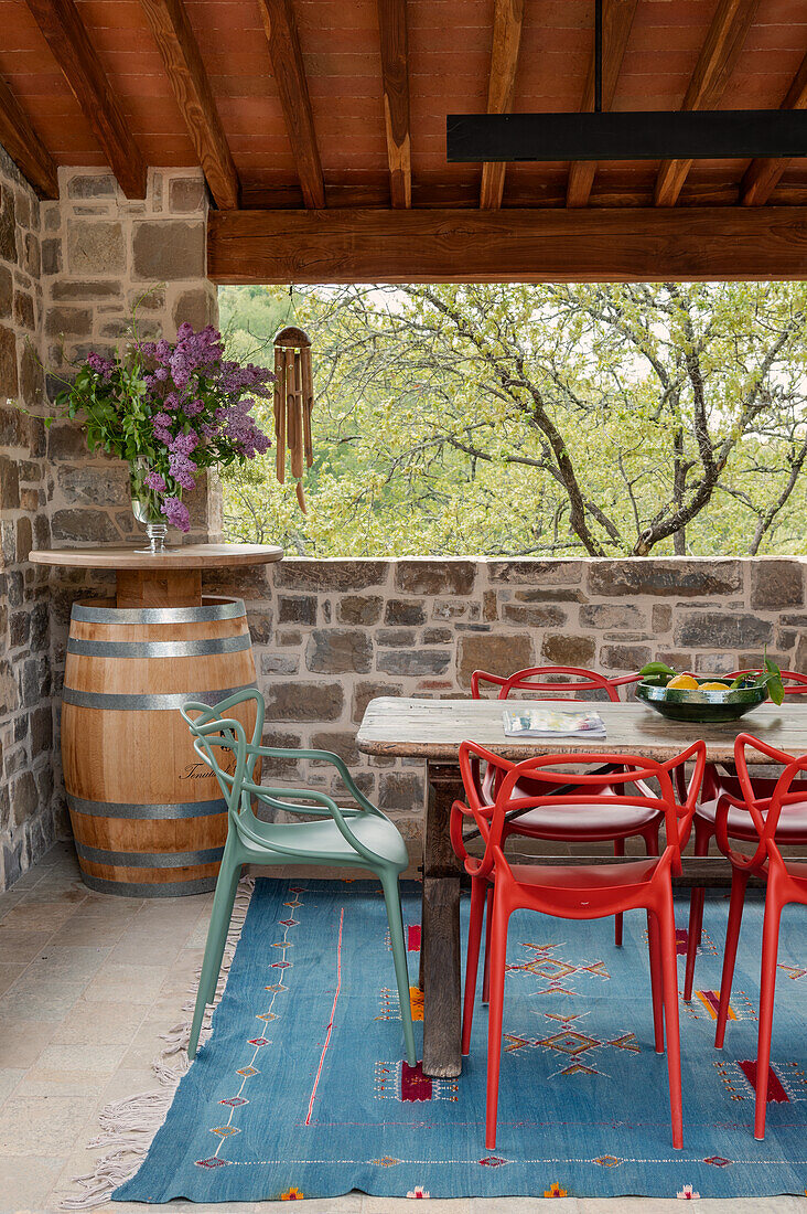 Essbereich auf der Terrasse mit farbenfrohen Stühlen, Holztisch und Weinfass