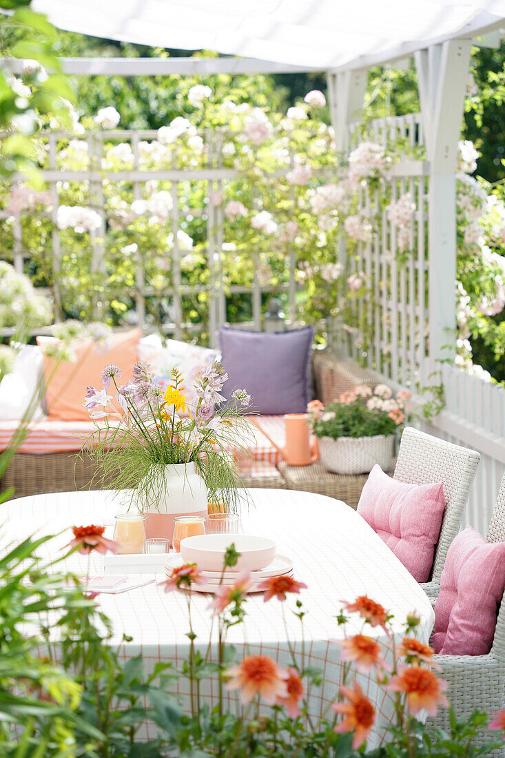 Blumengeschmückte Terrasse im Sommer mit Rattanmöbeln und Kissen in Pastellfarben