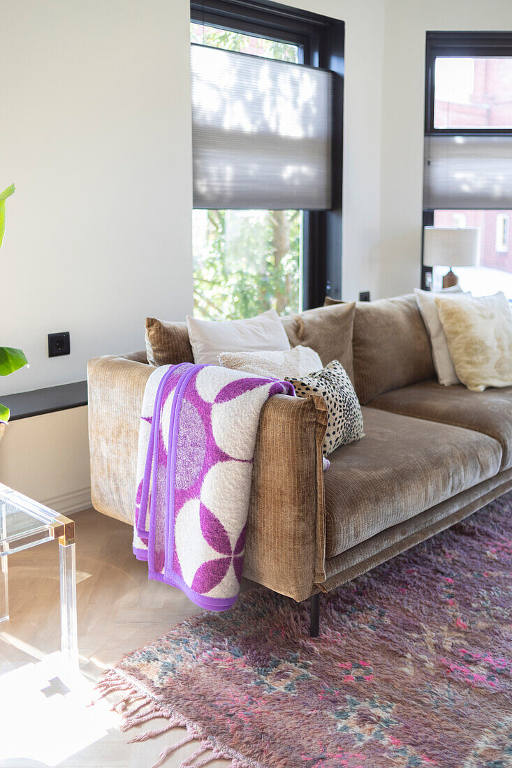 Light brown sofa with purple and white patterned blanket and colorful rug