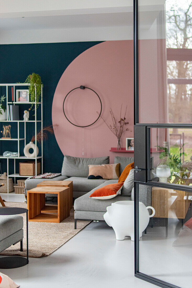 Modern living room with corner sofa, wall design in pink, wooden furniture and glass door