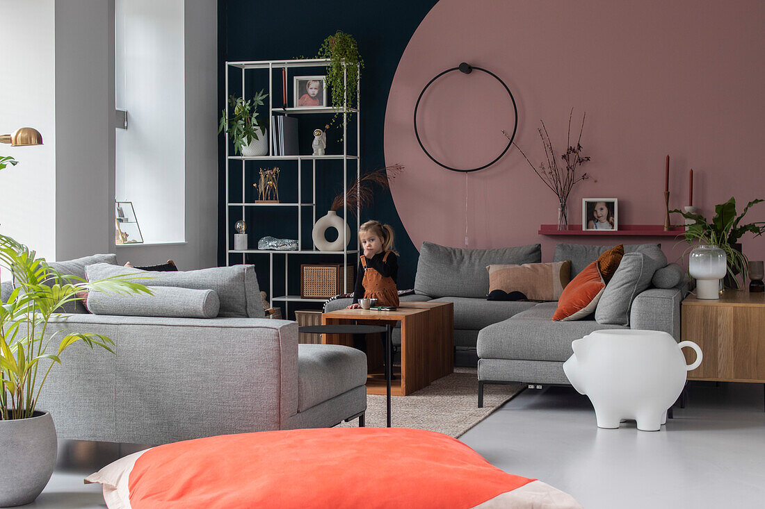 Kind im Wohnzimmer mit grauen Sofas, farbiger Akzentwand und offenem Regal