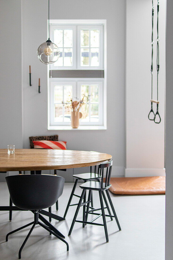 Round wooden table with black chairs in modern dining room with gymnastic rings