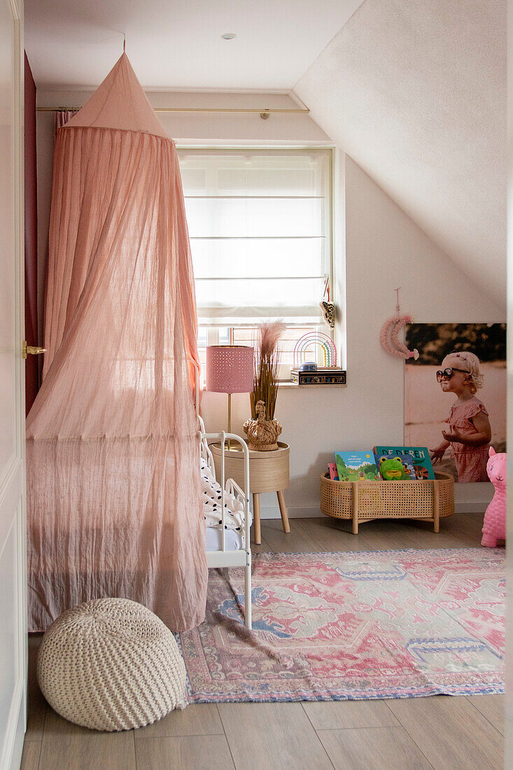 Children's room with pink canopy, bedside table and toy basket