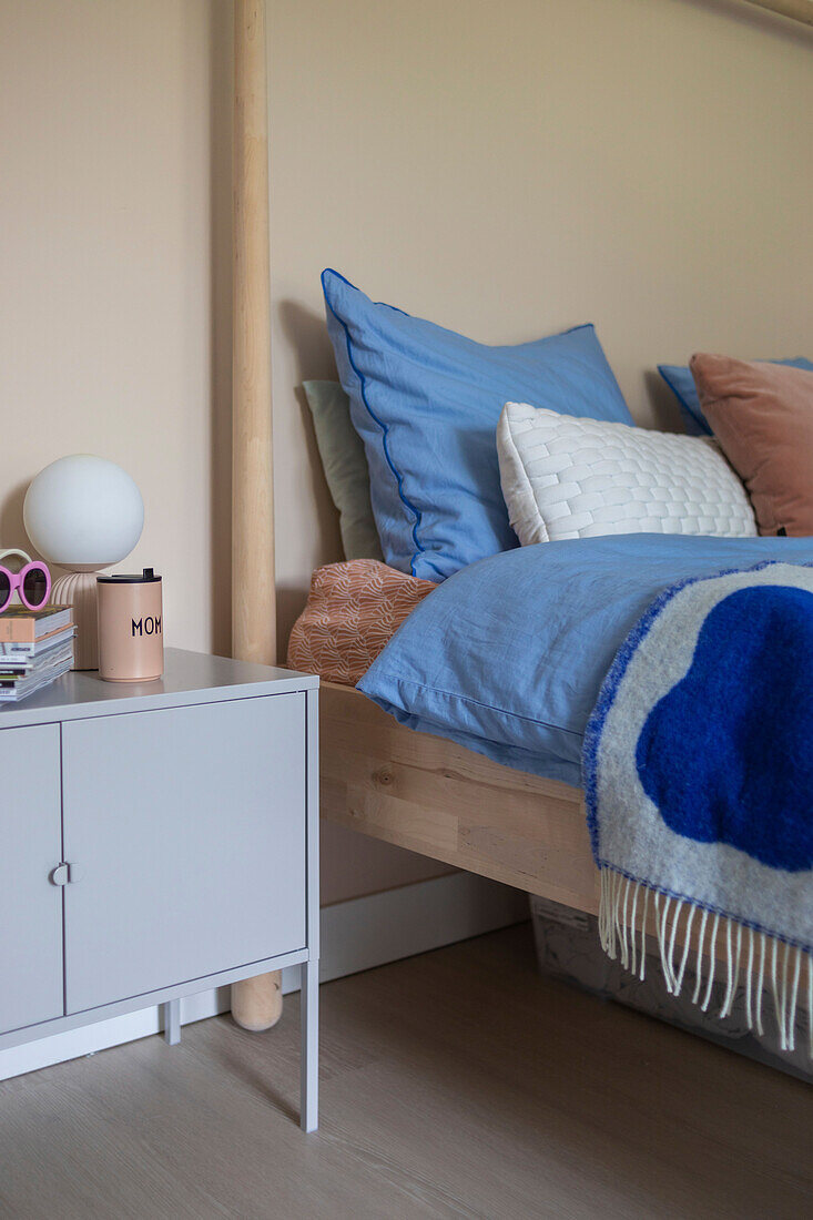 Wooden bed with blue bed linen, grey cupboard as bedside table