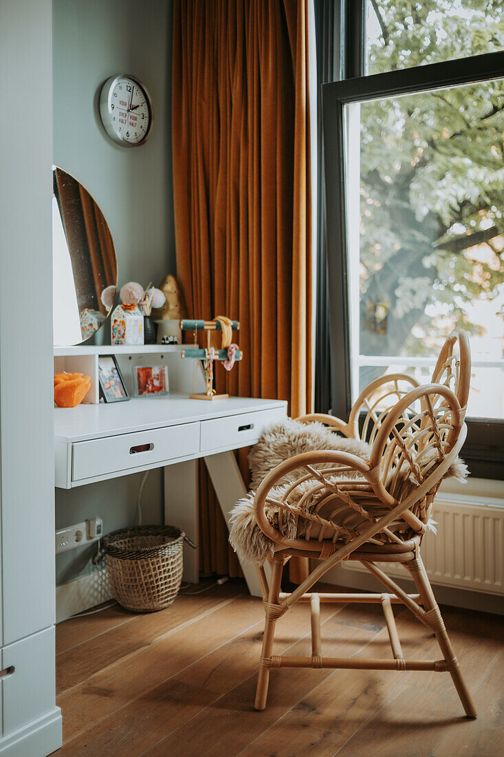 Dressing table with mirror and rattan chair in front of window with mustard-colored curtains