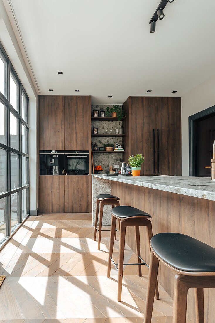 Kitchen with dark wooden cupboards, island and bar stools in front of floor-to-ceiling windows