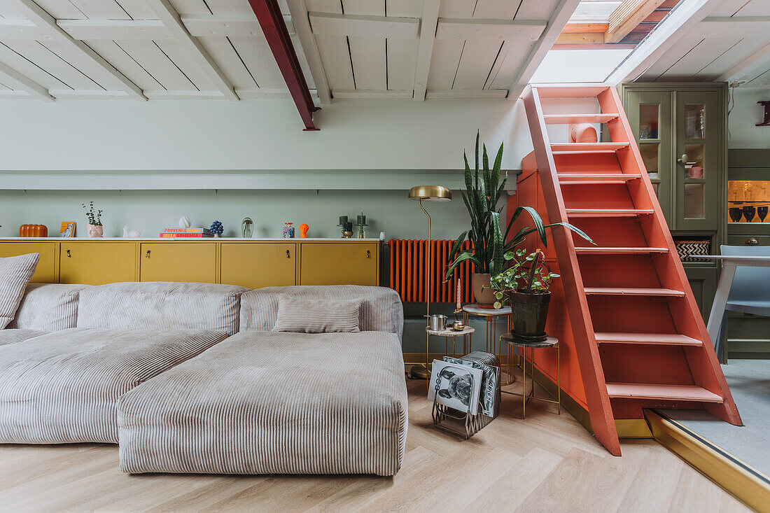 Living area with grey corduroy sofa, yellow cupboards and coral red stairs to the skylight