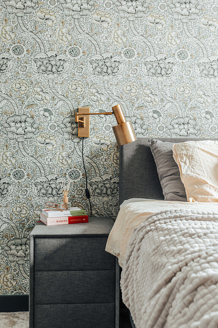 Gepolstertes Bett mit gemusterter Tapete und goldener Nachttischlampe im Schlafzimmer