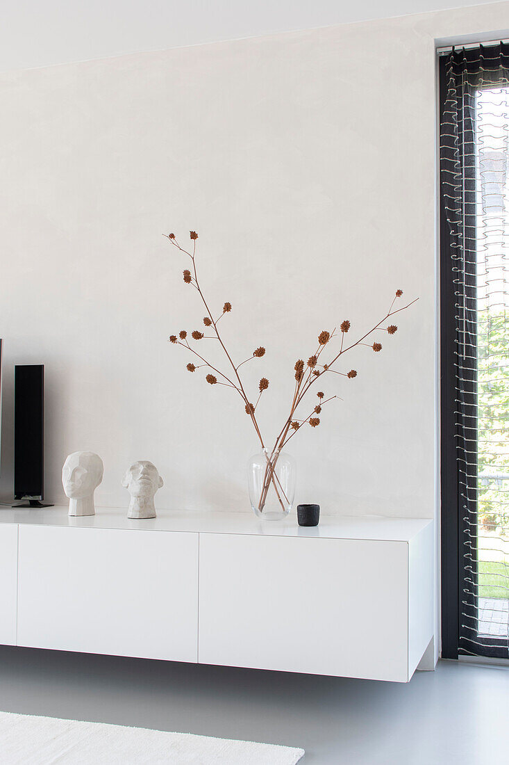 Schwebendes Sideboard mit minimalistischer Dekoration und Trockenblumen in Vase