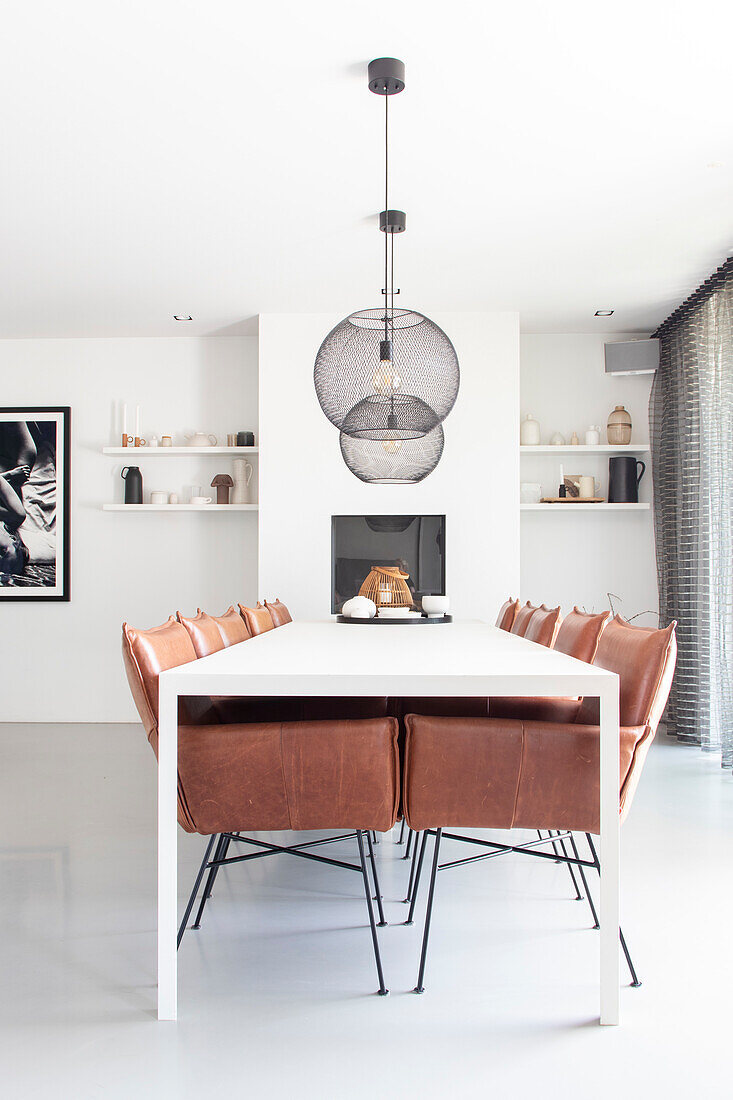 Dining room with long white table, brown leather chairs and black wire lights