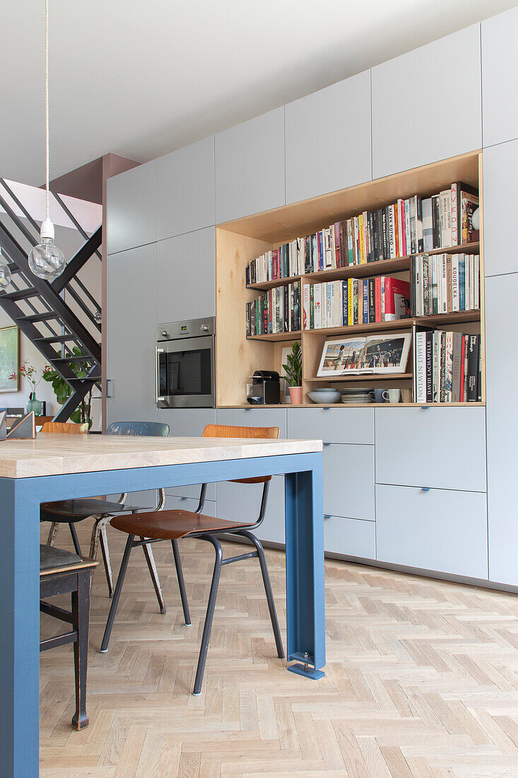 Offene Küche mit integrierter Bücherregalwand und Esstisch in Blau und Holzoptik