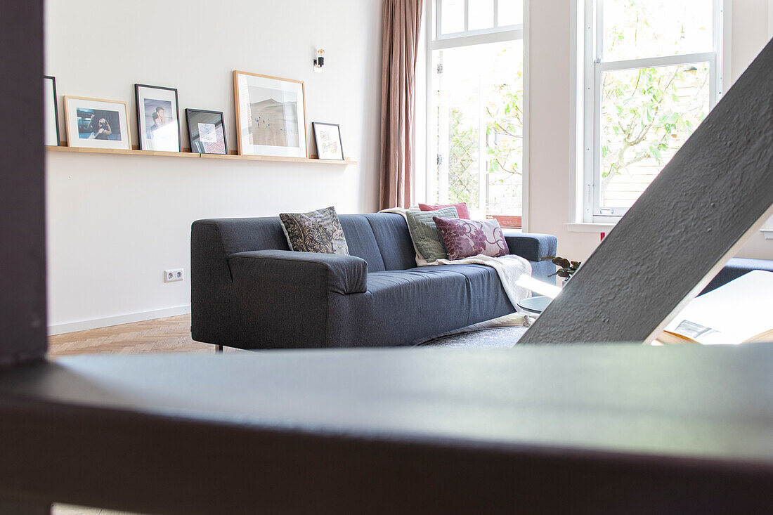 Graues Sofa mit gemusterten Kissen, Fensterfront und Bilderleiste im Wohnzimmer