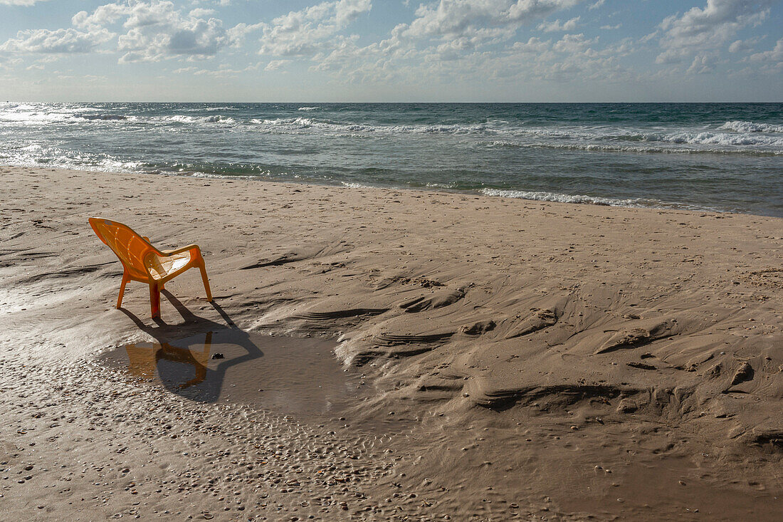 Plastic chair on sunny wet, sandy ocean beach, Bat Yam, Israel\n