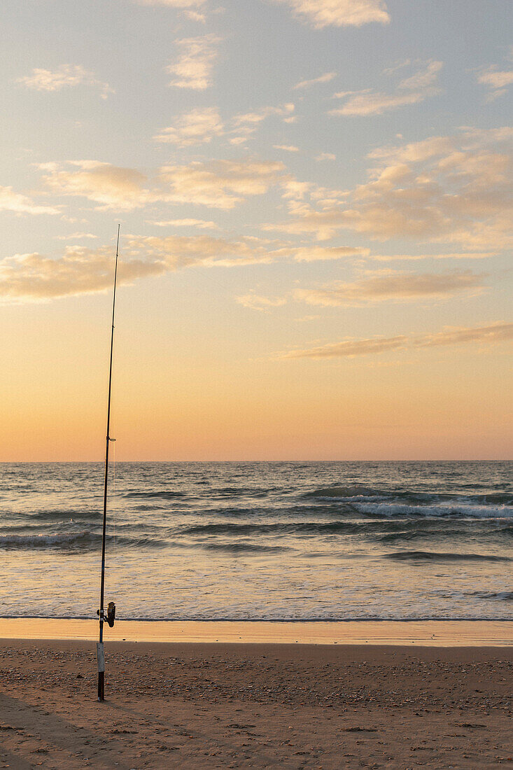 Angelrute im Sand am ruhigen Meeresstrand bei Sonnenuntergang, Bat Yam, Israel