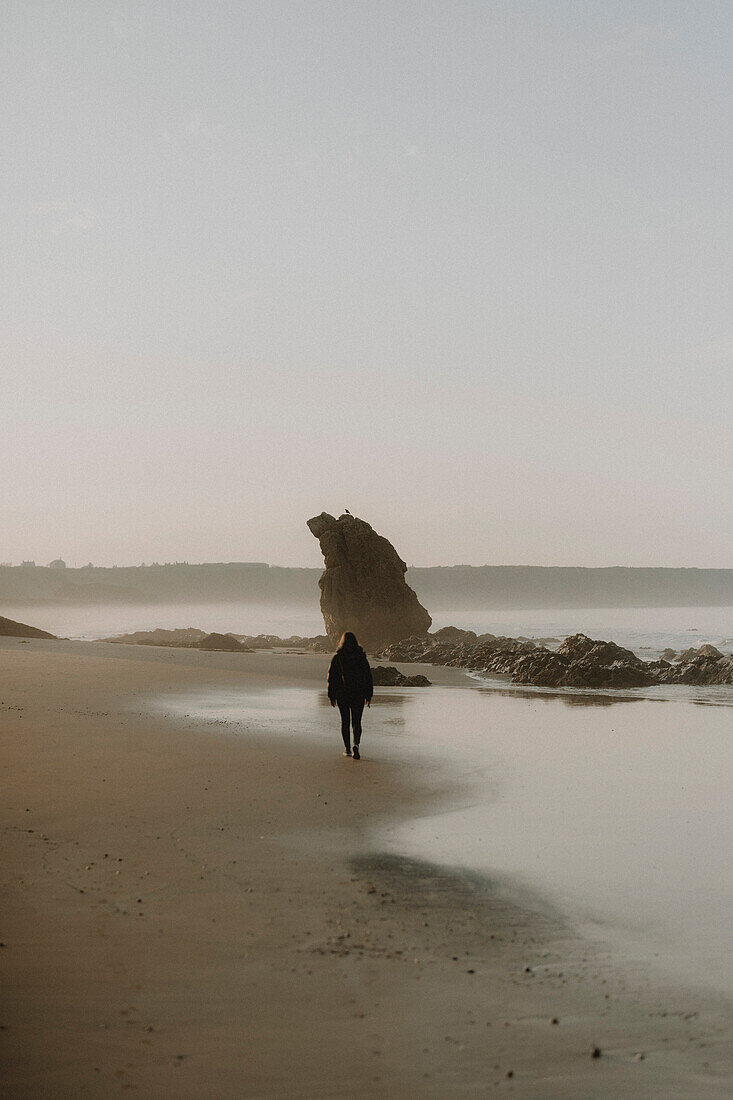 Woman walking on wet sand ocean beach at sunset, Cullen, Aberdeenshire, Scotland\n