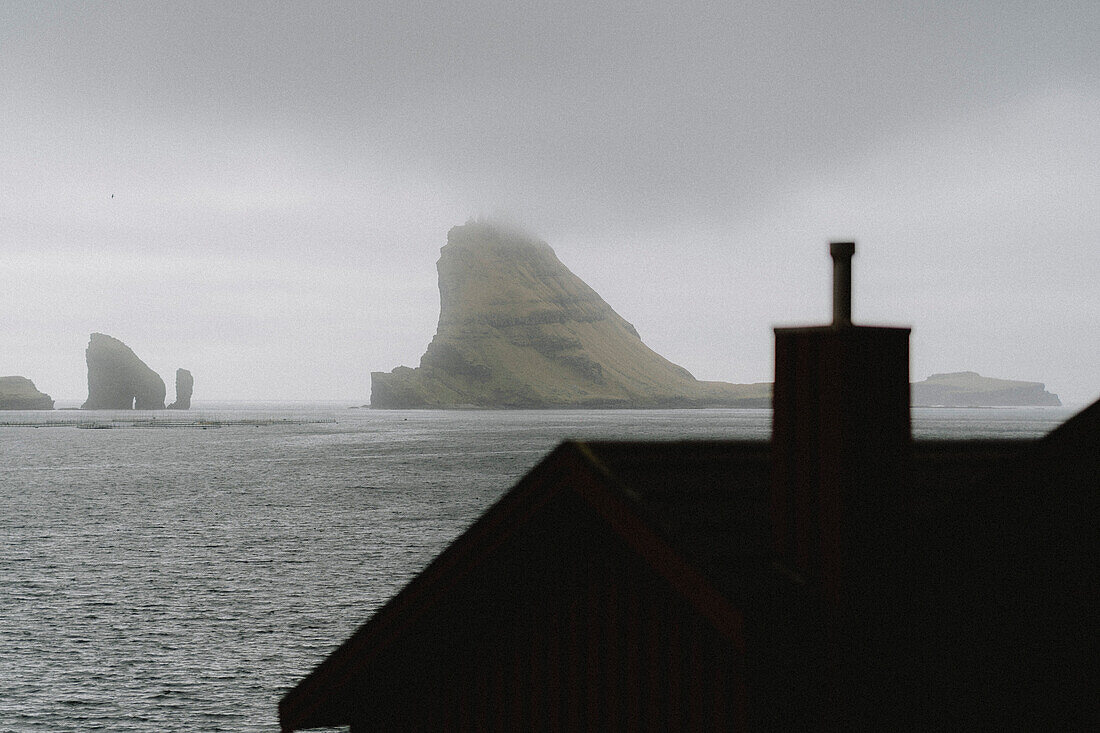 Rock formations beyond rooftop over sea, Bour, Vagar, Faroe Islands\n