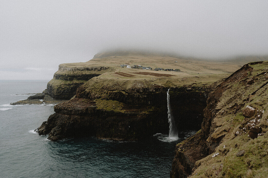 Waterfall flowing over cliff into sea, Gasadalur, Vagar, Faroe Islands\n