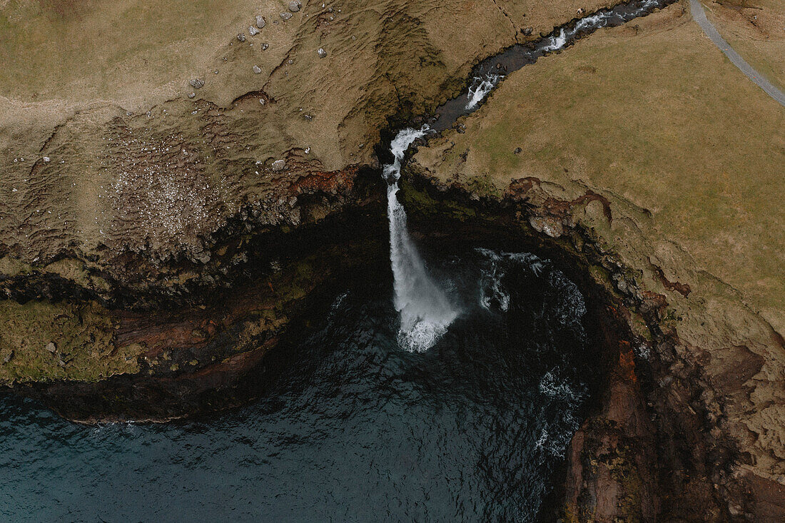 Aerial view waterfall flowing over cliff into sea, Gasadalur, Vagar, Faroe Islands\n