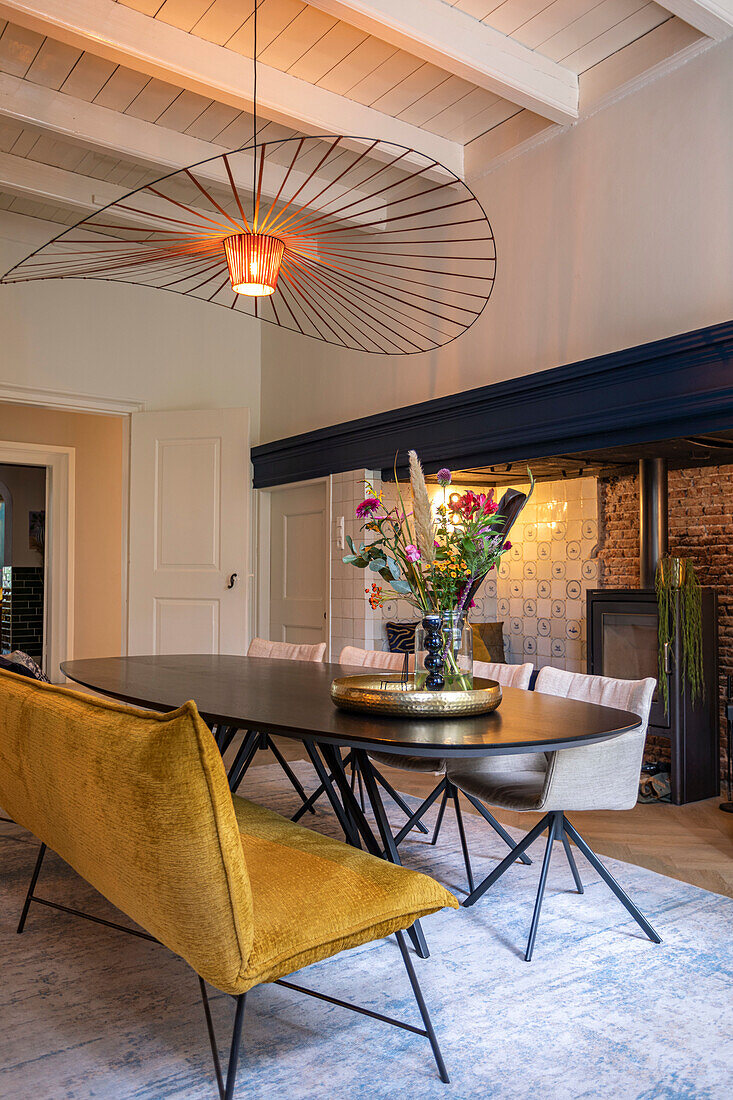 Dining room with oval wooden table, velvet bench and modern chandelier