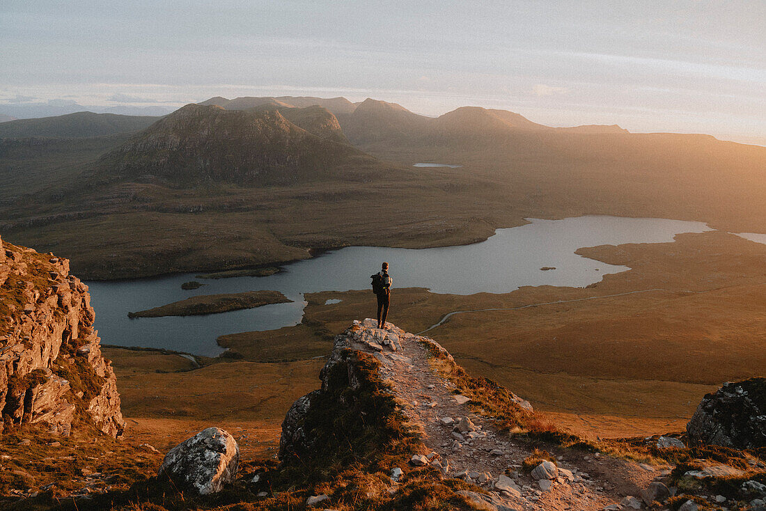 Hiker standing on mountain overlooking idyllic sunset view, Assynt, Sutherland, Scotland\n