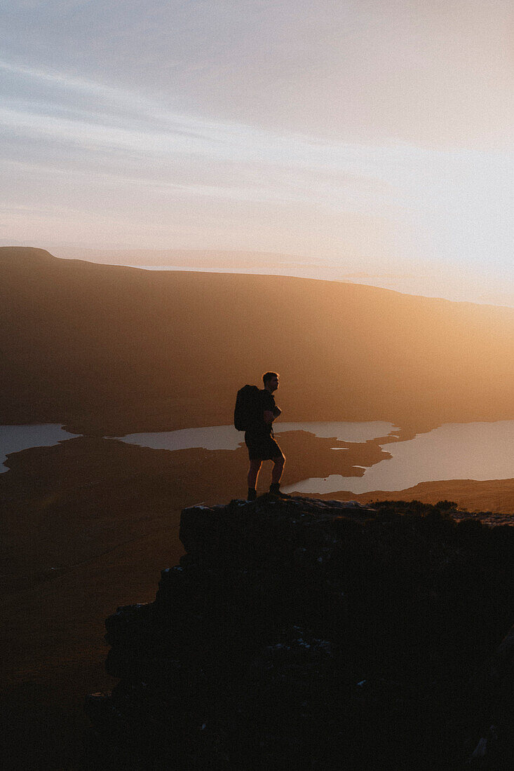 Silhouetted hiker on mountain at sunset, Assynt, Sutherland, Scotland\n