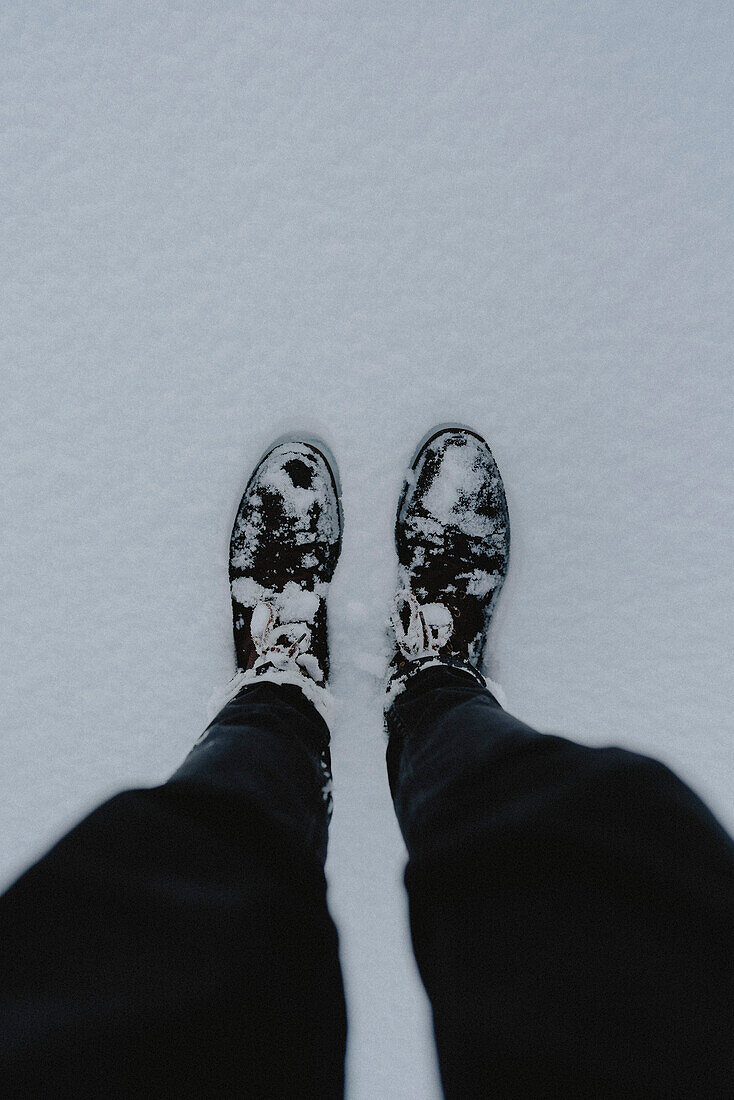 POV view from above legs of hiker in snowy hiking boots\n