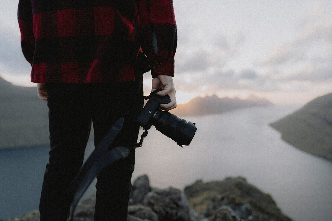 Photographer holding SLR camera on hill overlooking sea, Klakkur, Klaksvik, Faroe Islands\n