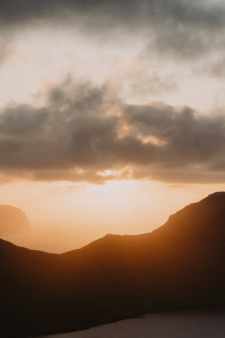 Sunset in clouds above ocean and silhouetted cliffs, Klakkur, Klaksvik, Faroe Islands\n