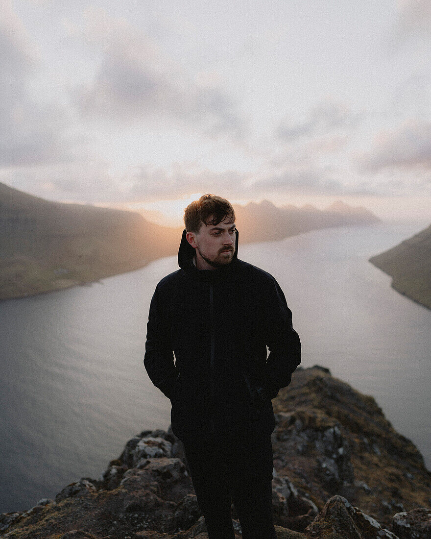 Wanderer auf einer Klippe über dem Fluss bei Sonnenuntergang, Klakkur, Klaksvik, Färöer Inseln